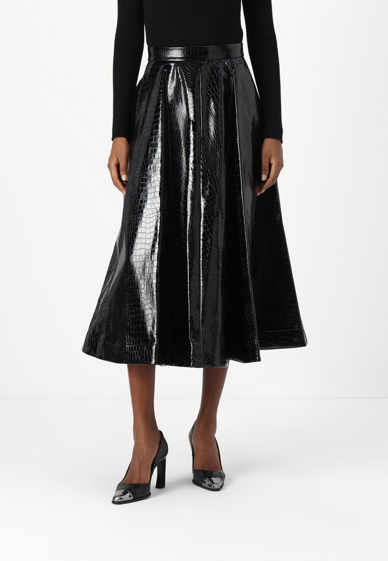 Falda midi plisada negra hecha de cuero sintético texturizado con acabado brillante que imita al cocodrilo, combinada con zapatos de tacón alto negros con acentos metálicos.