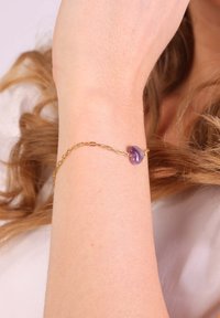Bracelet en chaîne dorée avec un accent en pierre violet irrégulière, surface texturée, maillons délicats et design minimaliste.