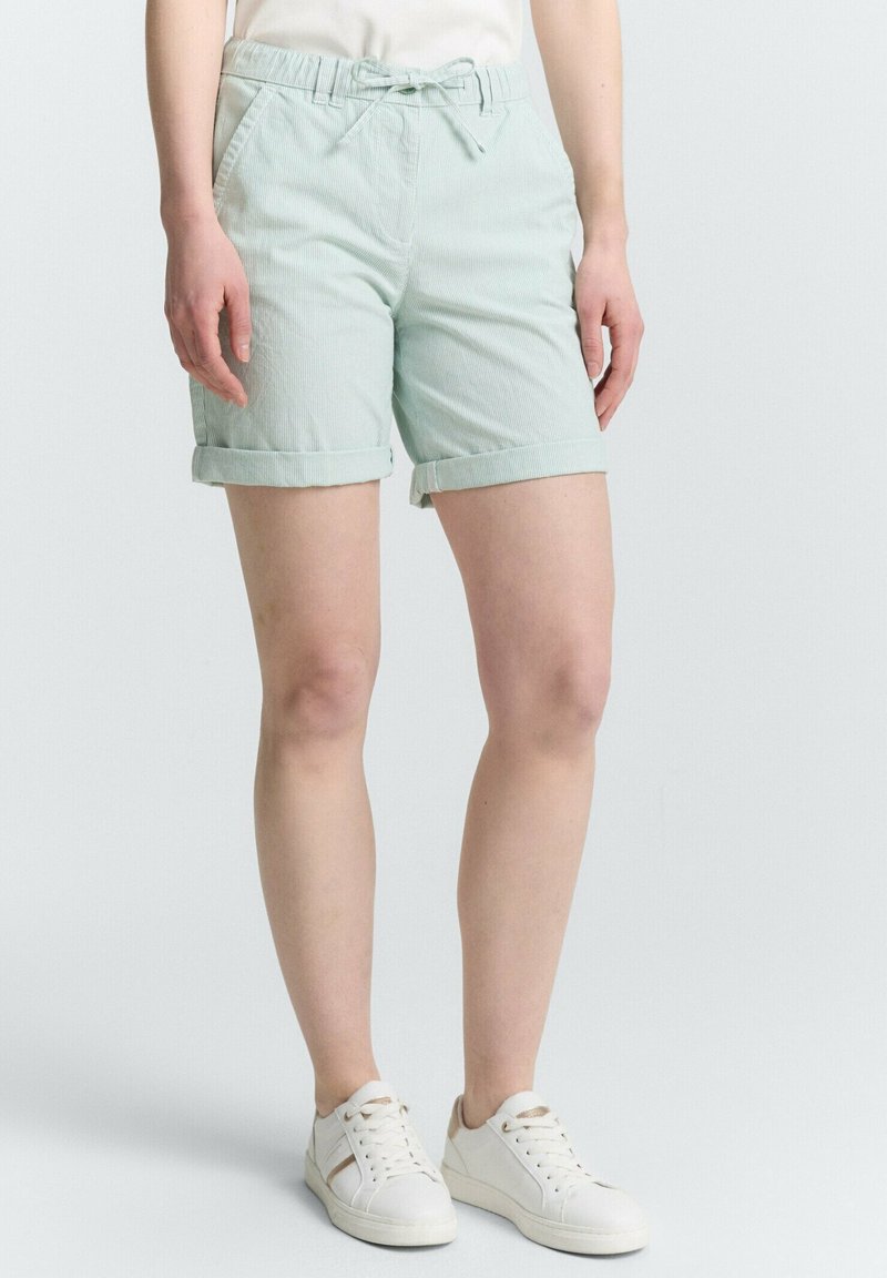 Shorts vert menthe clair en tissu texturé, avec taille élastique, lien de serrage et ourlets retournés. Portés avec des baskets blanches.