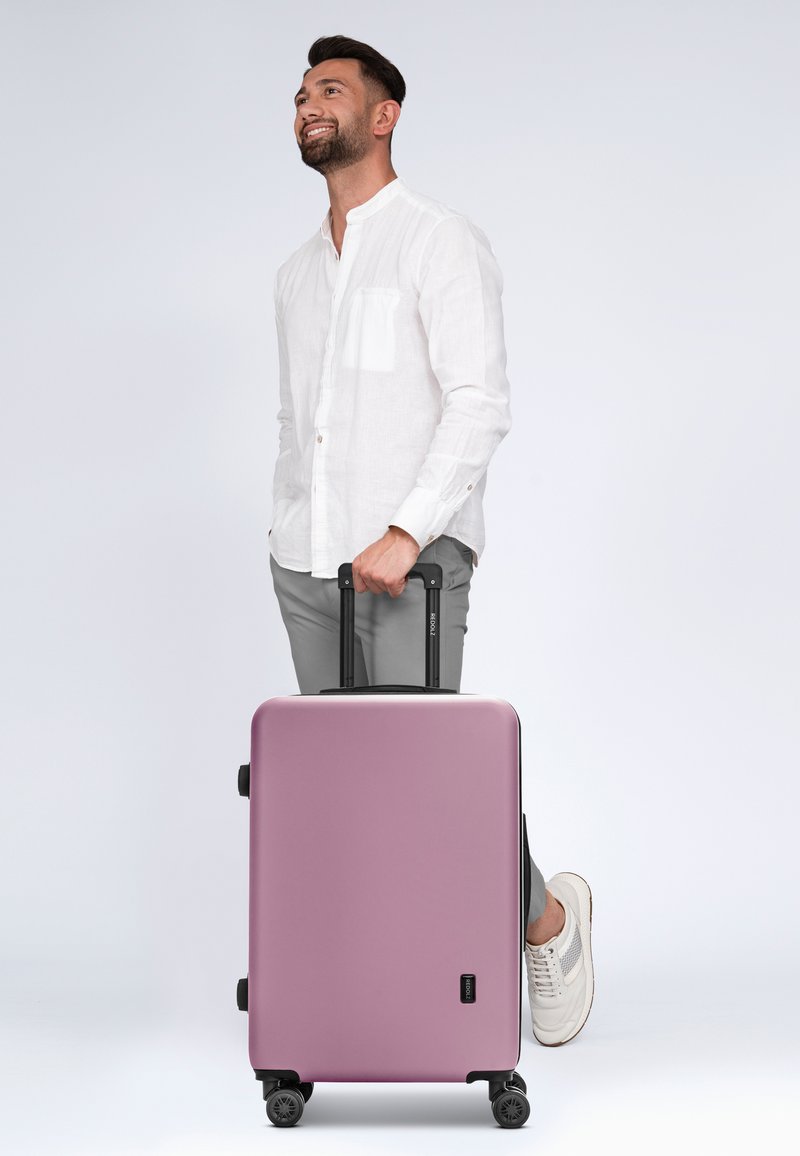 Maleta dura en un suave color metálico rosa con acentos negros, dos ruedas, mango extensible y forma rectangular.