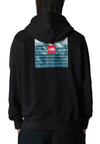 Sudadera con capucha negra que presenta un gran panel gráfico texturizado en azul y blanco en la parte posterior, con un logo rectangular rojo.