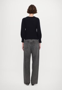 Schwarzer Strickpullover mit langen Ärmeln, kombiniert mit hochtaillierten, weiten, hellgrauen Jeans mit faded-Effekt, Rückenfächern und Kontrastnähten.