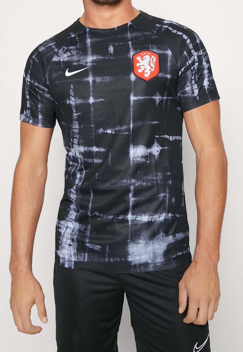 Camiseta deportiva negra de manga corta con un patrón texturizado de tie-dye en gris. Presenta un emblema de león rojo y el logo de Nike en el pecho.