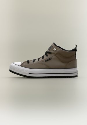 Zijaanzicht van een bruine hoge sneaker met zwarte veters, witte rubberen zool en zwart profiel op een neutrale achtergrond.