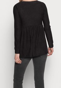 Černý dlouhý rukáv s texturovaným tečkovaným vzorem, přiléhavý korzet a nařasený pas. V kombinaci s tmavě šedými přiléhavými džíny.