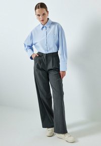Lichtblauw overhemd met knopen en een zak, gecombineerd met grijze broek met hoge taille en streepjespatroon en witte sneakers. Glad stof, ontspannen pasvorm.