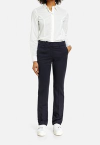 Marina byxor med skräddarsydd passform, sidofickor och bälteshällor, kombinerat med en vit långärmad skjorta med knappar. Vita sneakers fulländar looken.