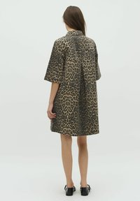 Beige en zwarte luipaardprint shirtjurk, met korte mouwen, oversized pasvorm, met een plooi aan de achterkant, gecombineerd met zwarte schoenen.