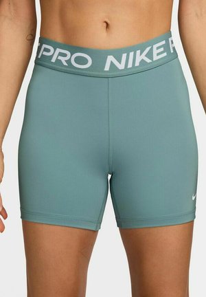 Donna che indossa pantaloncini a compressione Nike Pro color verde acqua a vita alta con logo bianco sulla fascia in vita e piccolo swoosh sulla coscia sinistra.
