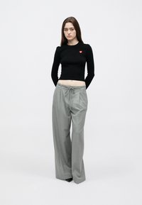 Top preto cropped de manga comprida com um patch de coração vermelho, combinado com calças largas cinza claro com cintura ajustável por cordão.