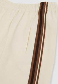 Krämfärgade sweatpants med elastisk midja har sidofickor och bruna randiga detaljer längs yttre sömmarna.
