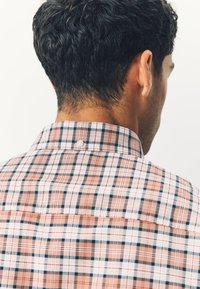 Chemise à carreaux avec col, présentant des motifs rouge, blanc et bleu marine. Détail de boutons au dos. Tissu léger avec une texture douce.