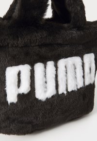 Svart faux fur-väska med vit fluffig "PUMA"-logotyp. Har två rundade handtag och en mjuk, texturerad yta. Kompakt rektangulär form.