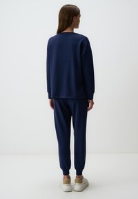 Felpa blu navy e pantaloni jogger in tessuto morbido, caratterizzati da una vestibilità rilassata, polsini a costine e vita elasticizzata, abbinati a sneakers bianche.
