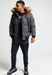 Halli puffer-jakk, millel on eemaldatav karvane kapuuts, lukuga taskud ja punased aksessuaarid, on kombineeritud mustade sörkjakkide pükste ja spordijalatsitega.