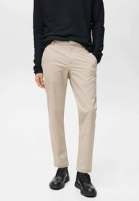 Beige trousers with a slim fit and flat front. Made of smooth fabric, paired with a black long-sleeve top and black sneakers.
