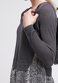 Pull en maille grise texturée à manches longues, avec un design court, associé à un bas à motif serpent.