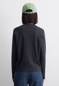 Sort langærmet skjorte med rund halsudskæring, glat tekstur, båret med blå jeans; suppleret med en lys grøn justerbar kasket.