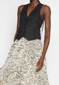 Sort, ærmeløs top med struktureret blomsterdesign, sat sammen med et flydende skørt med sort og hvidt abstrakt mønster.