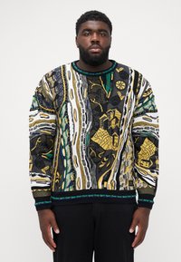 Pull en tricot avec un motif géométrique multicolore et des accents noir, blanc, vert et or. Col et poignets côtelés, design texturé.