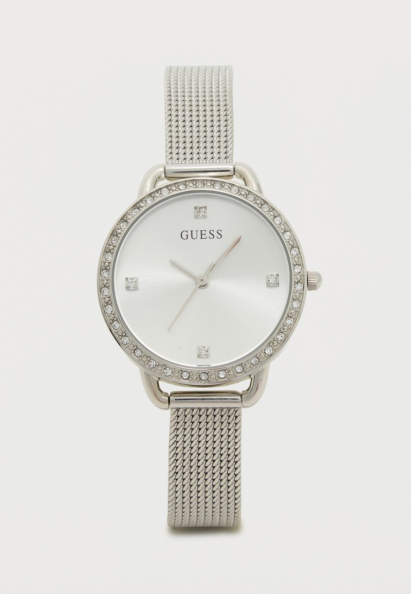 Relógio com pulseira de malha prata e mostrador redondo branco, adornado com cristais transparentes, apresentando ponteiros prateados e o logotipo da GUESS ao centro.