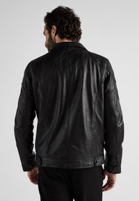 Zwarte leren jas met een gestructureerde afwerking, voorzien van een klassieke kraag, diagonale naden en drukknoopsluitingen in de taille.