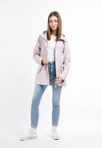 Lichtroze waterdichte jas met capuchon, zilveren beslag en ritszakken, gecombineerd met lichtblauwe jeans en witte sneakers.
