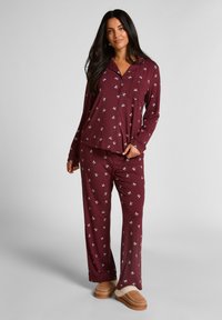 Bordeauxkleurig pyjamaset met een button-up top voorzien van een zak en een lange broek, beide versierd met een klein wit patroon. Zachte stof en ontspannen pasvorm.