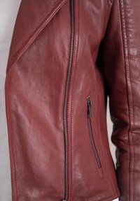 Burgundy leather jacket featuring a diagonal zipper, ribbed detailing on the sleeve, and a small zippered pocket on the arm.