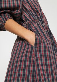 Marint rutig klänning med röda och gröna ränder, elastisk midja och sidofickor. Mjuk tyg med avslappnad passform och gathered ärmar.