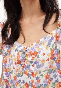 Chemisier fleuri en tissu léger et doux, avec des fleurs rouges, violettes, jaunes et vertes éclatantes ; il présente un détail froncé à l'avant et des manches dénudées.