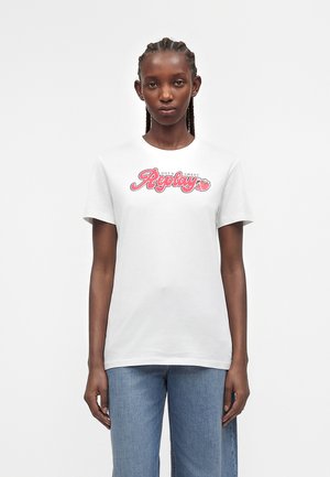 Femeie cu părul împletit purtând un tricou alb cu text roz „Replay Hot & Sweet” și un grafic cu căpșuni, asortat cu blugi albaștri.