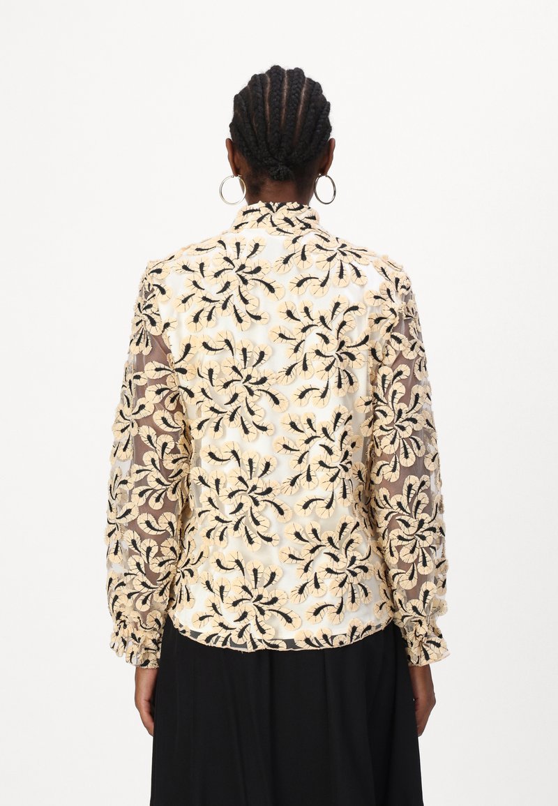 VezenBluza s cvjetnim uzorcima u crnoj boji na krem pozadini, s prozirnim rukavima i visokim ovratnikom.