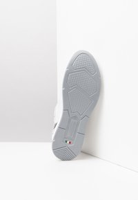 Semelle de sneaker blanche avec une surface en caoutchouc gris texturé, présentant des motifs géométriques et une étiquette indiquant "AeroGrattini" et la taille 37.