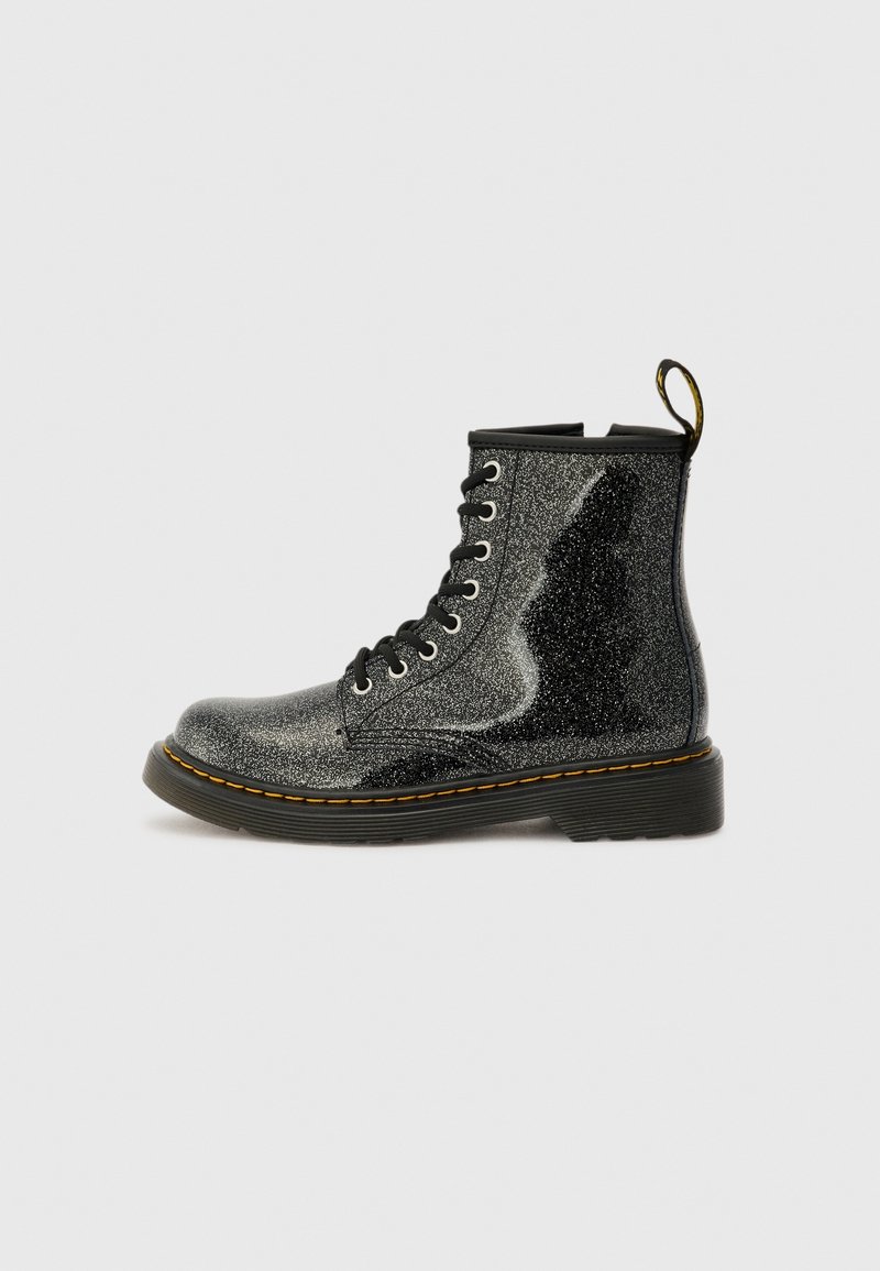 Botte de combat noire scintillante à lacets avec coutures jaunes et languette de tirage sur fond gris clair, vue de côté.