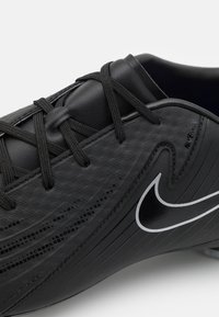 Fekete futballcipő, melynek texturált szintetikus felsőrésze van, kontrasztos ezüst Nike logóval és fekete fűzővel, letisztult dizájnnal.