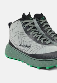 Grijs en zwarte sportschoenen met textuurstof, golvend design en groene accenten; beschikt over stevige zool met uitgesproken profiel voor grip.