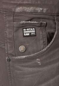 Grå denimjeans med sliten textur, som har en G-Star Originals-märkning, silverfärgad knappstängning och en avslappnad fickdesign.