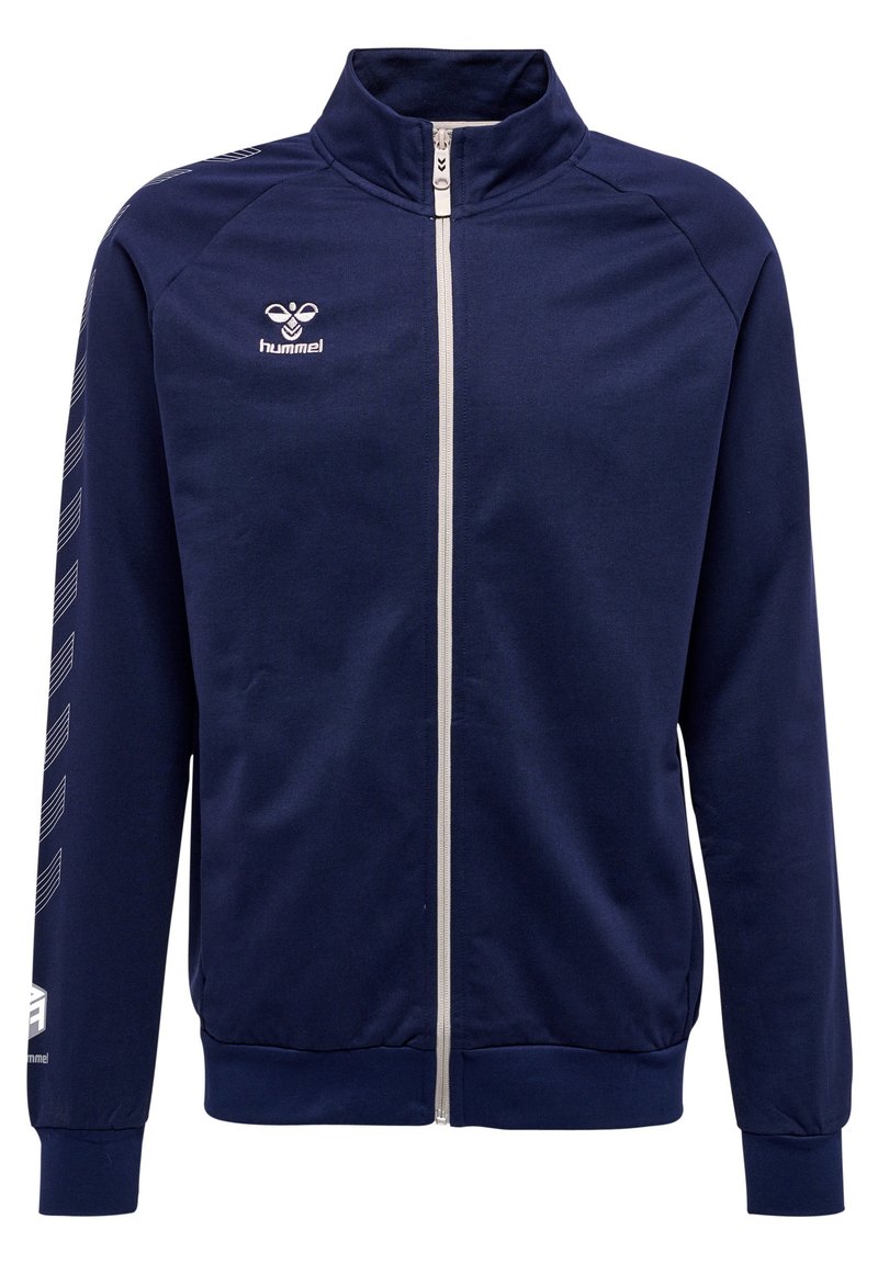 Marineblå zip-jakke lavet af glat stof. Har en høj krave, hvid lynlås og hvide chevronstriber på ærmerne. Hummel-logo på brystet.