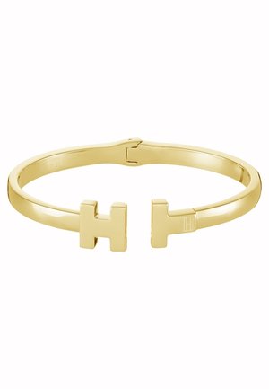Armbånd i guldtonet metal med åbne ender formet som to store bogstaver H, der vender mod hinanden.