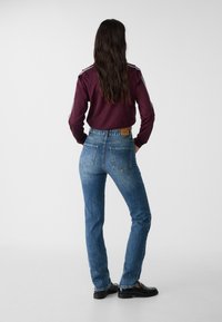 Högmidjade blåjeans i denimmaterial med en blekt finish, med bakfickor och en läderlapp, kombinerade med en vinröd topp.