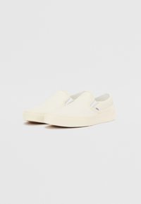 Pantofi slip-on din pânză albă, cu accente elastice pe laterale și talpă din cauciuc plat. Design minimalist, fără modele sau ornamente vizibile.