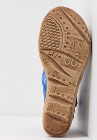 Ošoupaná hnědá podrážka boty s texturovanými grip vzory, označení velikosti 37 a částečně viditelný modrý svršek na bílém pozadí.