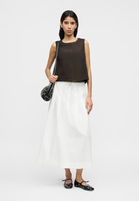 Καφέ κοντό αμάνικο τοπ, σε συνδυασμό με μια λευκή μακριά φούστα. Τα αξεσουάρ περιλαμβάνουν μια μικρή μαύρη τσάντα και μαύρα επίπεδα παπούτσια.