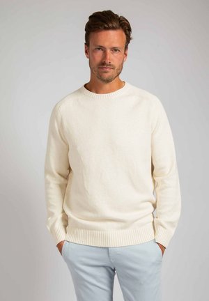 Helles cremefarbenes, gestricktes Sweatshirt mit Rundhalsausschnitt, gerippten Bündchen und Saum; getragen über hellblauen Hosen aus einem strukturierten, weichen Stoff.