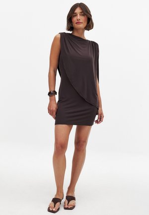 Dark brown sleeveless dress with draped design, lightweight fabric, and a relaxed fit. Worn with dark sandals and a chunky bracelet.