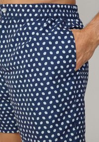 Marineblaue Badeshorts mit hellblauen Punkten, elastischem Bund, Seitentasche und weichem Stoff. 