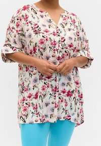 Květinová blůza vyrobená z lehk�é látky, zdobená růžovými a modrými květy na krémovém pozadí, s knoflíkovým výstřihem a volnými, krátkými rukávy.