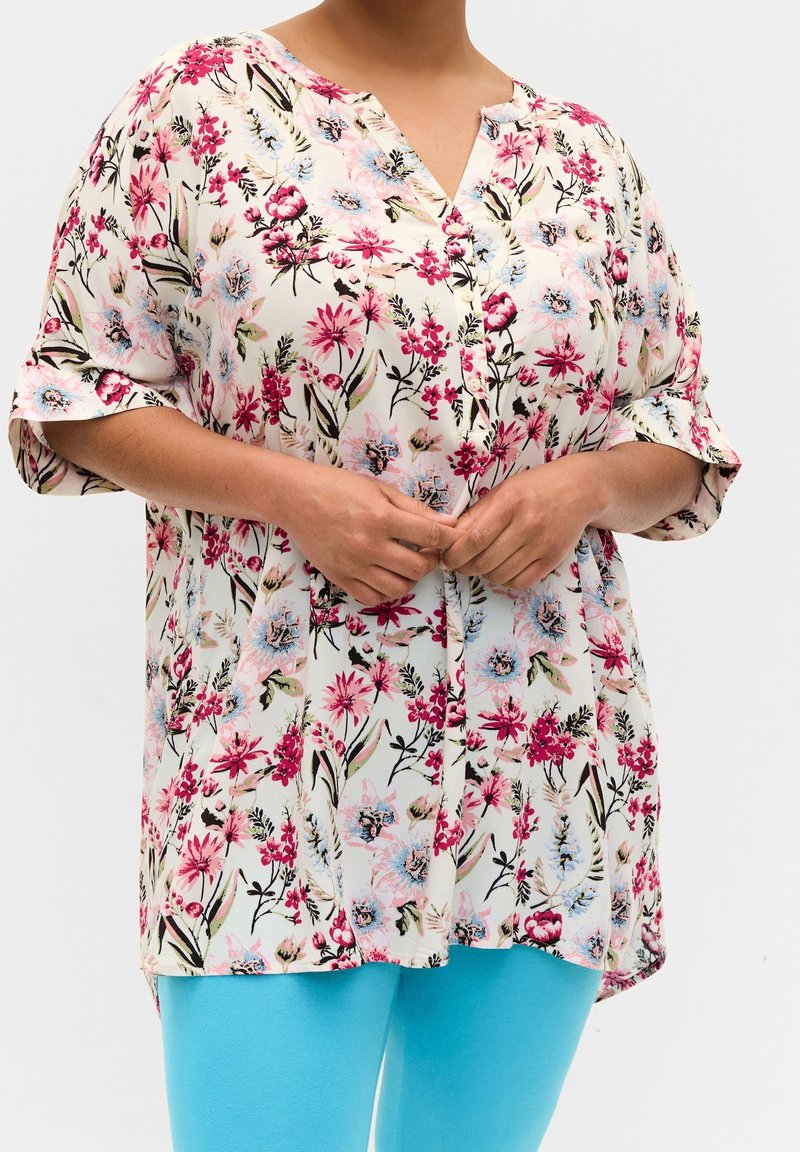 Květinová blůza vyrobená z lehké látky, zdobená růžovými a modrými květy na krémovém pozadí, s knoflíkovým výstřihem a volnými, krátkými rukávy.