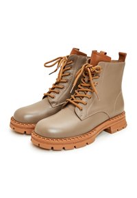 Bottines en cuir beige avec une finition texturée, à bout rond, lacées marron, et une semelle en caoutchouc épaisse couleur beige avec un bord à motifs.